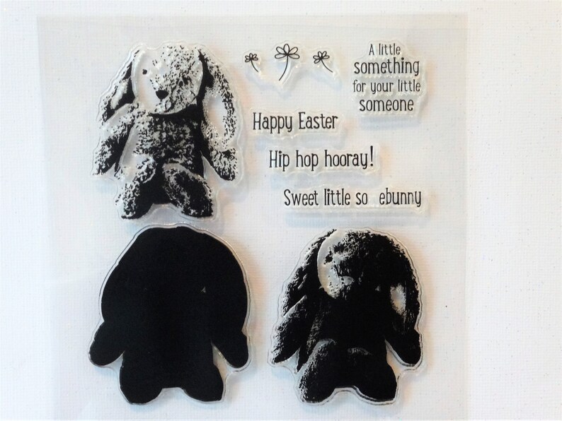 May include: A set of four clear rubber stamps featuring a bunny rabbit design. The stamps include a bunny rabbit with a textured surface, a bunny rabbit outline, and two text stamps that read "Happy Easter" and "Hip hop hooray! Sweet little so ebunny".