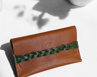 Puede incluir: Una cartera de cuero marrón con una correa trenzada verde.