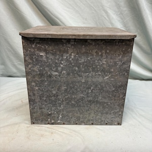 Peut inclure: Un bac de rangement en m&eacute;tal galvanis&eacute; avec un couvercle &agrave; charni&egrave;re. Le bac a une forme rectangulaire et une finition gris argent&eacute; mouchet&eacute;. Le couvercle est d'une nuance de gris plus claire. L'objet semble vintage ou antique.
