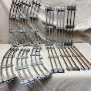 May include: A collection of vintage metal toy train tracks. The set includes curved and straight track pieces, showing signs of age and use. The tracks are silver-toned with a weathered appearance, suggesting they are from an older toy set.
