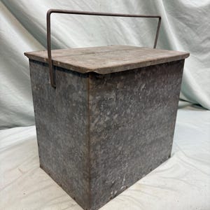 Peut inclure: Un conteneur rectangulaire en m&eacute;tal galvanis&eacute; avec un couvercle et une poign&eacute;e. Le conteneur a une surface textur&eacute;e et une forme rectangulaire. La poign&eacute;e est en m&eacute;tal et est fix&eacute;e au couvercle. Le conteneur est probablement utilis&eacute; pour le stockage.