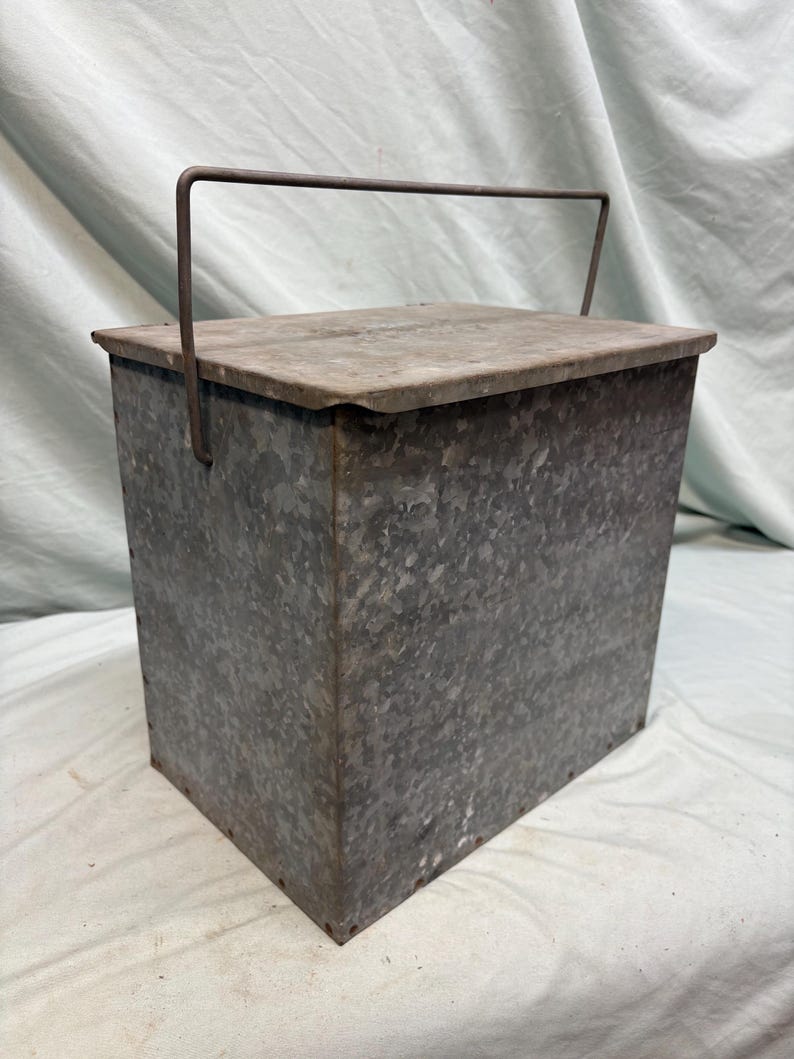 Peut inclure: Un conteneur rectangulaire en m&eacute;tal galvanis&eacute; avec un couvercle et une poign&eacute;e. Le conteneur a une surface textur&eacute;e et une forme rectangulaire. La poign&eacute;e est en m&eacute;tal et est fix&eacute;e au couvercle. Le conteneur est probablement utilis&eacute; pour le stockage.