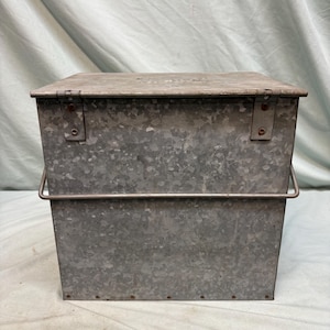Peut inclure: Un conteneur de stockage en m&eacute;tal galvanis&eacute; rectangulaire avec un couvercle &agrave; charni&egrave;re et une poign&eacute;e en fil de fer. Le m&eacute;tal a un aspect mouchet&eacute; et gris. La surface du conteneur est l&eacute;g&egrave;rement textur&eacute;e.