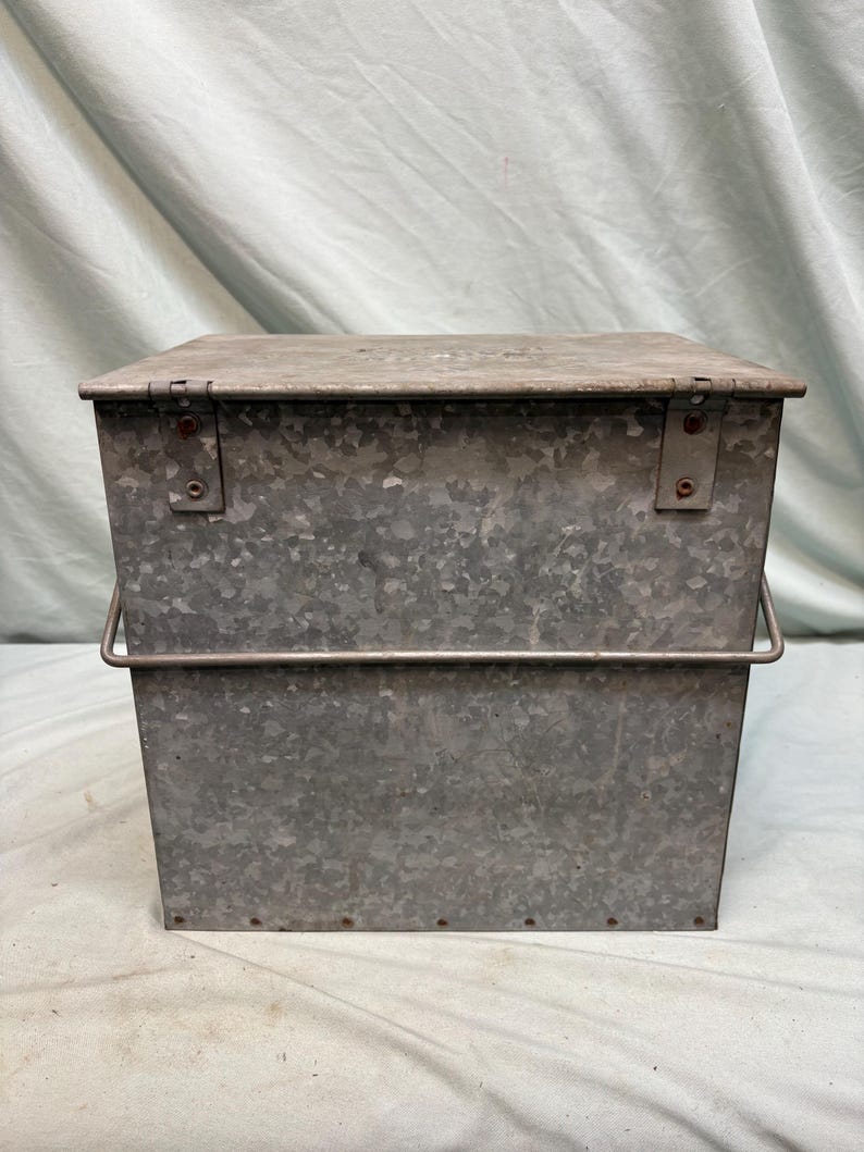 Peut inclure: Un conteneur de stockage en m&eacute;tal galvanis&eacute; rectangulaire avec un couvercle &agrave; charni&egrave;re et une poign&eacute;e en fil de fer. Le m&eacute;tal a un aspect mouchet&eacute; et gris. La surface du conteneur est l&eacute;g&egrave;rement textur&eacute;e.