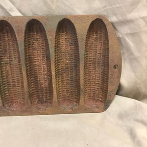 May include: A vintage cast iron cornbread pan with five individual molds. The pan is brown and has a rustic appearance.