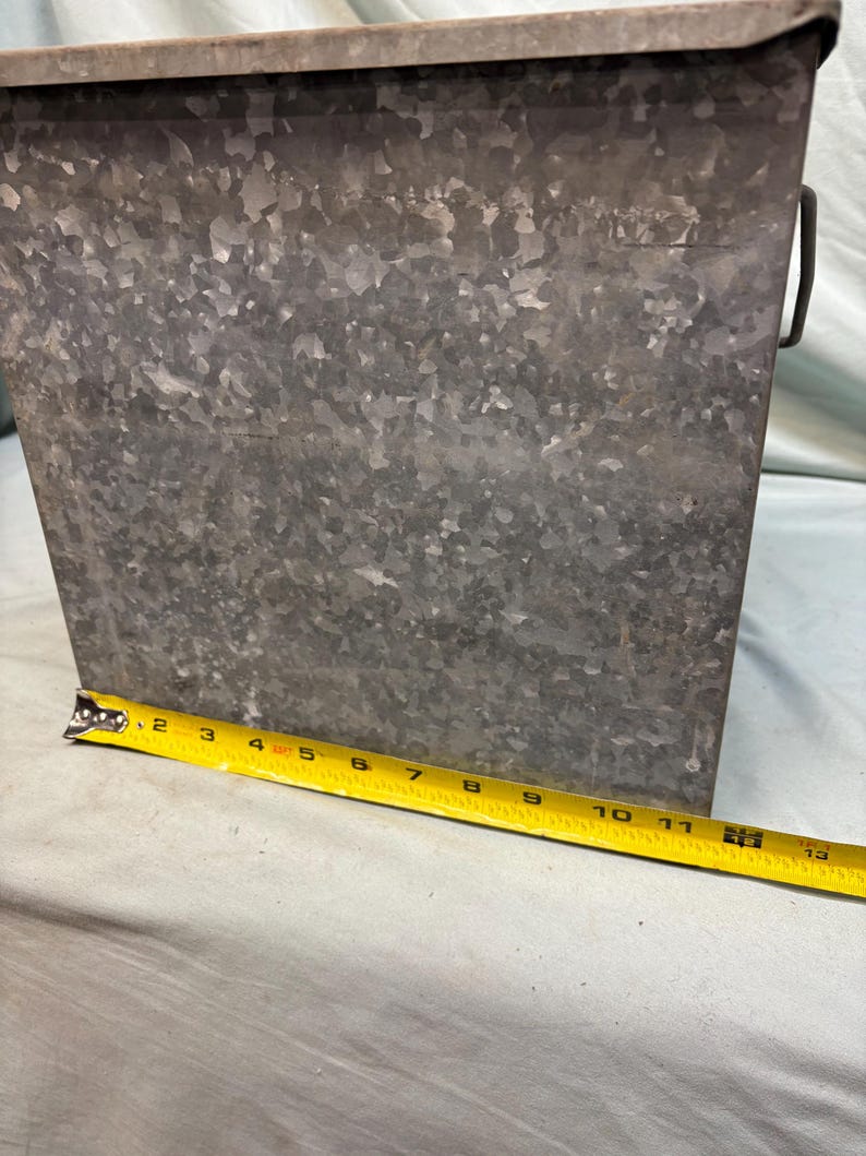 Peut inclure: Un seau rectangulaire en m&eacute;tal galvanis&eacute; avec une poign&eacute;e. Le seau mesure environ 30 cm de haut et a une surface textur&eacute;e. Un ruban &agrave; mesurer jaune est plac&eacute; &agrave; c&ocirc;t&eacute; du seau.