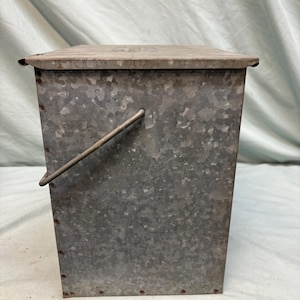 Peut inclure: Un conteneur en m&eacute;tal galvanis&eacute; avec un couvercle et une poign&eacute;e. Le conteneur rectangulaire a une surface textur&eacute;e et est rivet&eacute;. Le couvercle est pos&eacute; &agrave; plat sur le dessus. La poign&eacute;e est en m&eacute;tal et est fix&eacute;e sur le c&ocirc;t&eacute;.