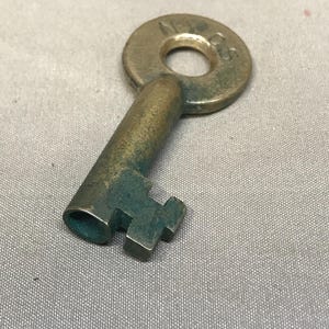 May include: A vintage brass key with a circular head and a rectangular bit. The key shows signs of age with a greenish patina on the shaft and bit. The head of the key has the letters "N-3" stamped on it.