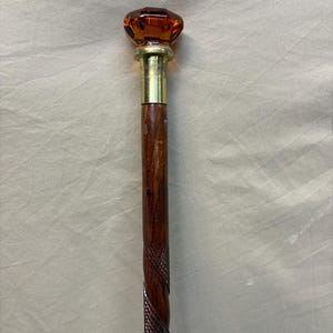 May include: A vintage walking cane with a faceted amber-colored glass knob handle. The handle is attached to a brass collar and a dark brown wooden shaft with a carved spiral design. The cane is a classic accessory.