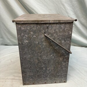 Peut inclure: Un seau rectangulaire en m&eacute;tal galvanis&eacute; avec un couvercle &agrave; charni&egrave;re et une poign&eacute;e en fil de fer. Le seau a une surface tachet&eacute;e et textur&eacute;e et est con&ccedil;u pour le stockage. Le couvercle est plat et chevauche l&eacute;g&egrave;rement les c&ocirc;t&eacute;s.