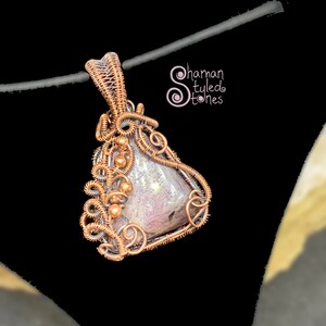 May include: A copper wire wrapped pendant featuring a pink and white iridescent stone. The pendant is in the shape of a teardrop and has a copper wire loop at the top for hanging.