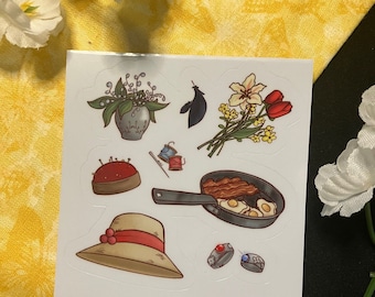 May include: A sheet of stickers featuring various illustrations, including a bouquet of flowers, a hat, a pan of bacon and eggs, a sewing pincushion, and a vase of lilies.