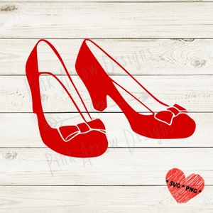 May include: A pair of red ruby slippers with bows. The slippers are on a white wood background.