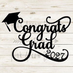 Może przedstawiać: Czarna dekoracja z czapką absolwenta i napisem "Congrats Grad 2027" ozdobną czcionką. Projekt umieszczono na tle białego drewna, idealny na uroczystości ukończenia szkoły.