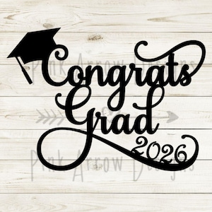 May include: Black graduation-themed sign with the words "Congrats Grad 2026" in a cursive font. A graduation cap is on the left side of the text. The background is a light wood grain pattern.