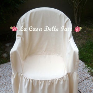 May include: A white chair cover with a ruffled bottom. The cover has the text "La Casa Delle Fate" printed on the front.