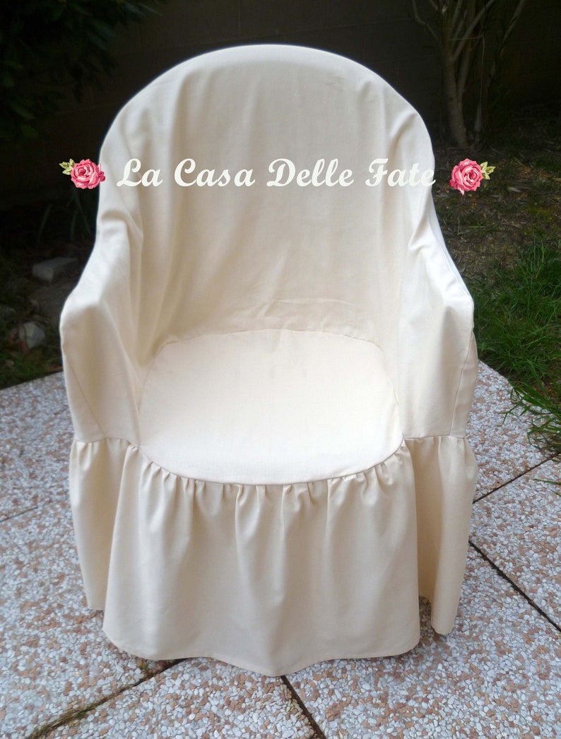 May include: A white chair cover with a ruffled bottom. The cover has the text "La Casa Delle Fate" printed on the front.