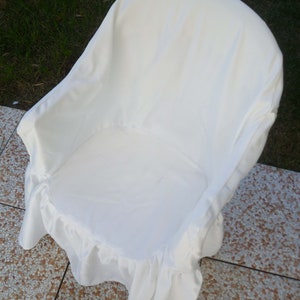 May include: White chair cover with a ruffled edge. The cover is made of a soft, white fabric and is designed to fit over a standard chair.