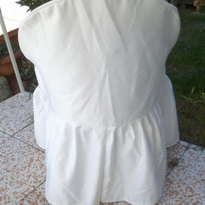 May include: White chair cover with a ruffled bottom. The cover is made of a smooth, white fabric.