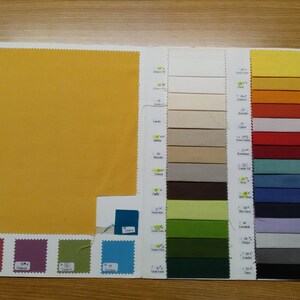 May include: A fabric swatch book featuring a range of colours, including yellow, orange, red, green, blue, and grey. The swatches are organised in rows and columns, with each swatch labelled with a number and name.