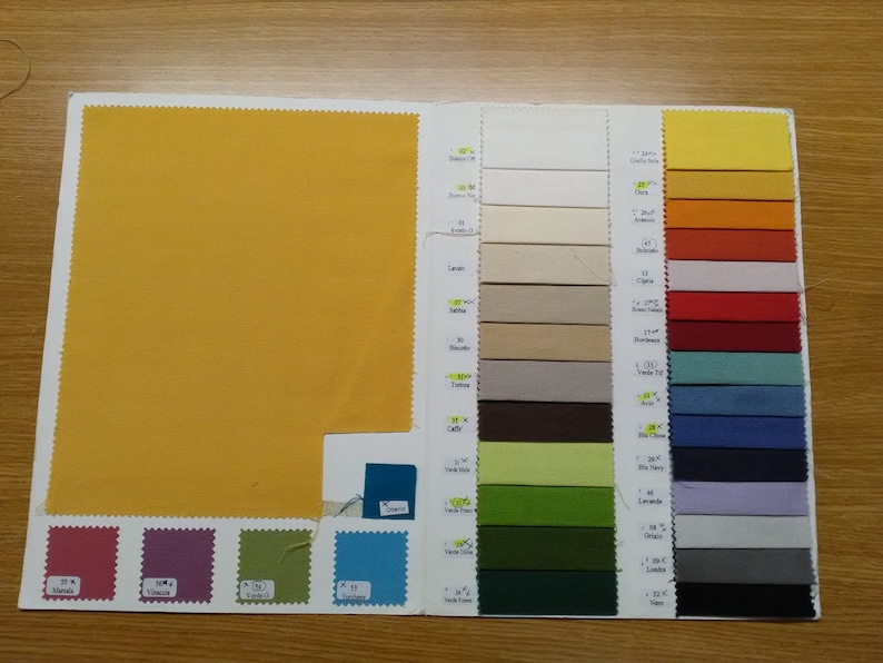 May include: A fabric swatch book featuring a range of colours, including yellow, orange, red, green, blue, and grey. The swatches are organised in rows and columns, with each swatch labelled with a number and name.