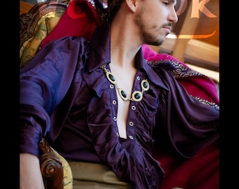 May include: A purple satin shirt with ruffled trim and a gold and black necklace. The shirt has long sleeves and is paired with beige pants. A gold leaf headpiece is also visible. The text on the image reads "The Stellar shirt in Purple Satin and the Erikurr pants in Beige."