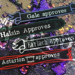May include: Four embroidered patches with black fabric and white text. The patches feature the names Gale, Halsin, Karlach, and Astarion, each followed by the word "approves". The patches are on a sparkly purple and silver background.