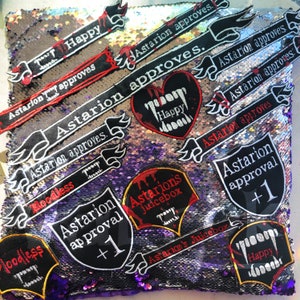 Peut inclure: Un coussin en sequins argentés et violets avec plusieurs patchs brodés. Les patchs présentent le texte "Astarion approuve" et "Astarion approbation +1".