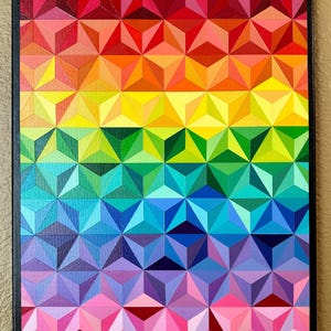 Puede incluir: Una vibrante pintura abstracta geométrica que presenta un espectro de colores del rojo al violeta. La obra de arte se compone de formas triangulares tridimensionales repetidas, creando un efecto texturizado. El lienzo está enmarcado en un borde negro.
