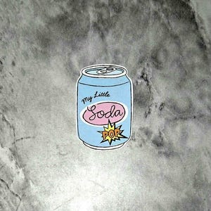 May include: A light blue soda can sticker with the words "My Little Soda" in a pink oval and a yellow "POP" burst graphic. The can has a silver top and is outlined in black.