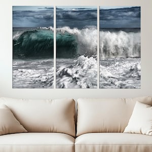 Puede incluir: Impresión en lienzo de tres paneles que representa una poderosa ola del océano. La ola es de un color verde azulado intenso, con espuma y rocío blancos. El cielo está cubierto de nubes oscuras. Se muestra sobre un sofá beige.