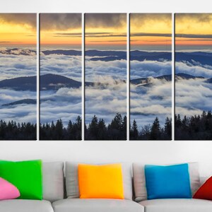 May include: A five-panel canvas print depicting a mountain landscape at sunrise. The scene features layers of mountains partially obscured by a sea of clouds, with a vibrant orange and yellow sky above. Dark green trees line the bottom.