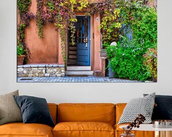 May include: A blue door with a white frame is surrounded by lush green vines and foliage. The door is set into a brick wall with a stone walkway leading up to it.
