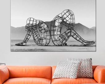 May include: Black and white photograph of a metal sculpture of two figures, one larger than the other, sitting back to back. The figures are made of wire mesh and are posed in a contemplative manner. The sculpture is set against a backdrop of mountains.