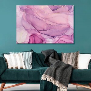 May include: Abstract painting with pink and purple swirls and gold accents. The painting is framed and hanging on a teal wall above a green velvet sofa.