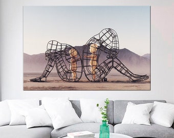 May include: A black metal sculpture of two figures, one larger than the other, standing in a desert landscape. The figures are made of wire mesh and appear to be embracing.