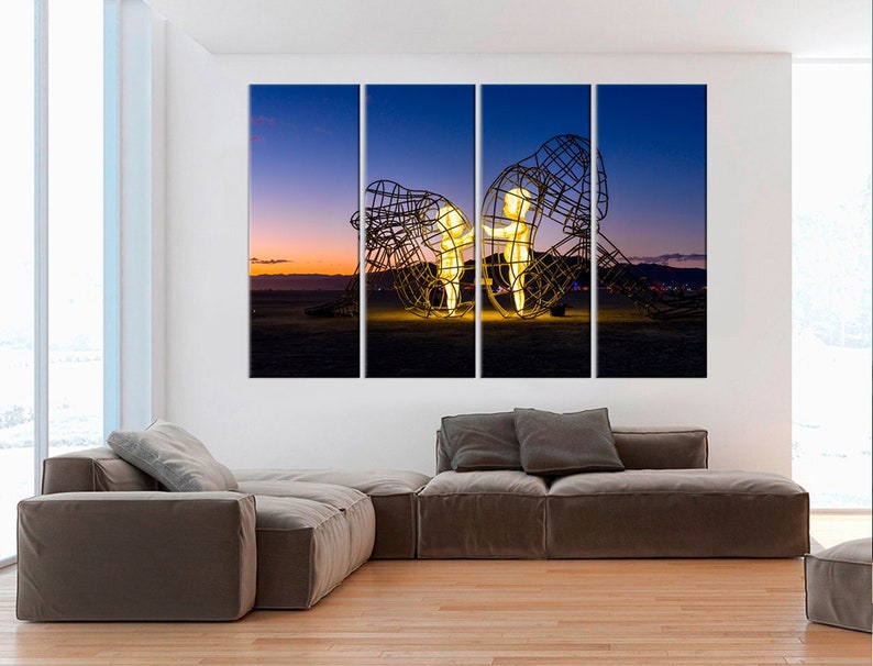 May include: A three-panel canvas print featuring a glowing metal sculpture of two figures standing inside a larger, abstract metal structure. The sculpture is set against a backdrop of a purple and orange sunset sky.