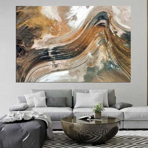 Könnte beinhalten: Große abstrakte Leinwandkunst mit einem fließenden Design in Braun-, Beige-, Schwarz- und Weißtönen. Das Kunstwerk hat ein strukturiertes Aussehen, das einer Landschaft oder geologischen Formation ähnelt. Die Leinwand ist über einem grauen Sofa montiert.