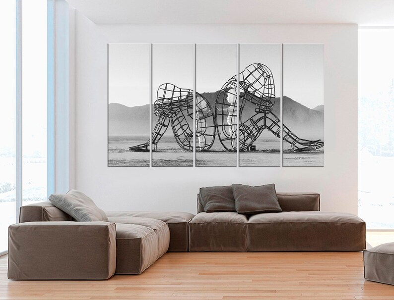 May include: Black and white photograph of a large metal sculpture of two figures intertwined. The sculpture is in a desert landscape.