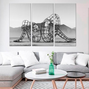May include: A black and white photograph of a metal sculpture of two figures intertwined. The sculpture is in a desert landscape.