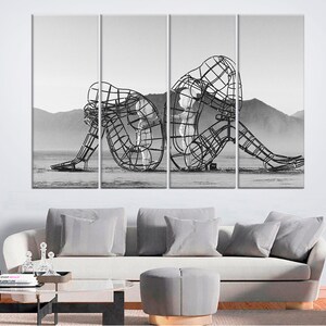 May include: A black and white photograph of a metal sculpture of two figures, one sitting and the other standing, in a desert landscape.