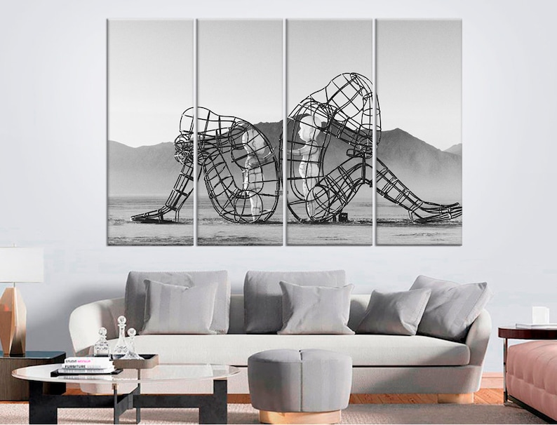 May include: A black and white photograph of a metal sculpture of two figures, one sitting and the other standing, in a desert landscape.