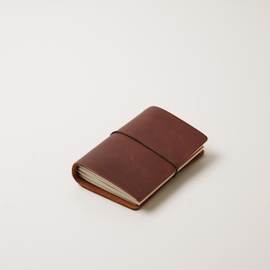 Peut inclure: Un journal en cuir marron avec une fermeture élastique noire. Le journal rectangulaire contient des pages blanches. La couverture est de couleur marron foncé. C'est un article de papeterie.