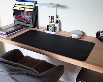 May include: A wooden desk with a black desk mat, a white lamp, a white pen holder with pens and pencils, a gray chair, and a vintage camera.