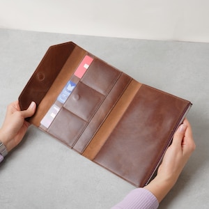 May include: A brown leather wallet with a fold-over flap and magnetic closure. The interior features multiple vertical card slots containing various cards and a large open compartment on the right side secured with a silver-toned metal zip.
