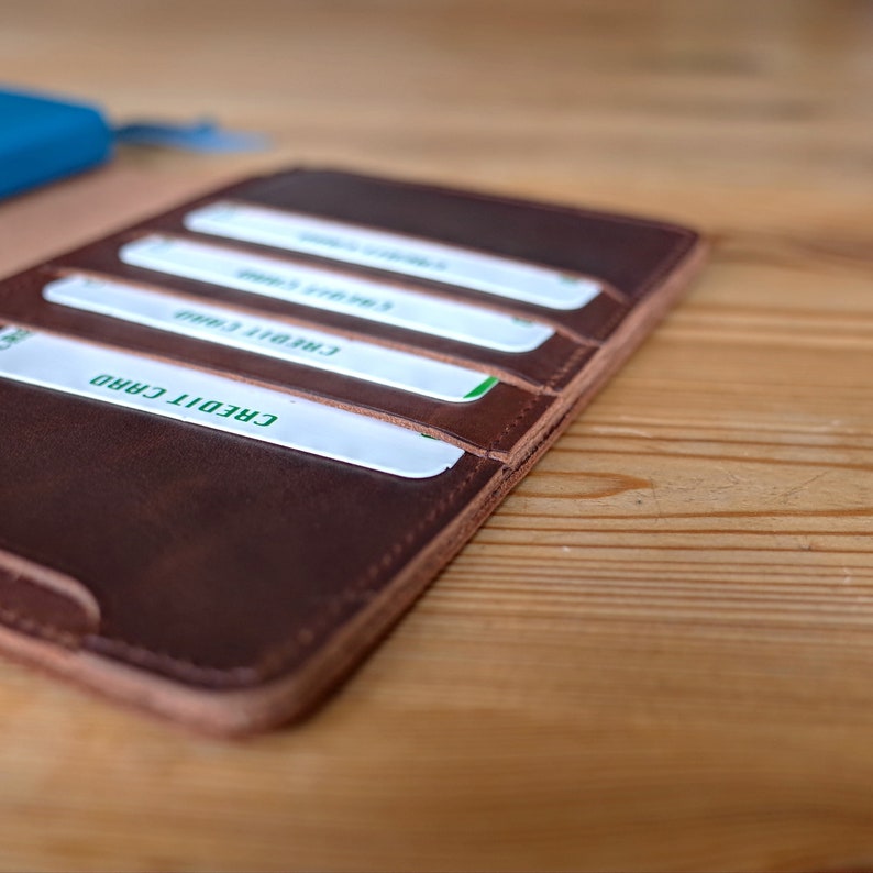 May include: A brown leather wallet with multiple slots for credit cards. The wallet is open and the slots are filled with white cards with green text.