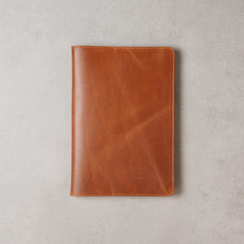 Peut inclure: Une couverture de journal ou de carnet en cuir brun clair de forme rectangulaire. La couverture est d'une couleur brun moyen chaud avec un grain et une texture visibles. Les bords sont soigneusement cousus.