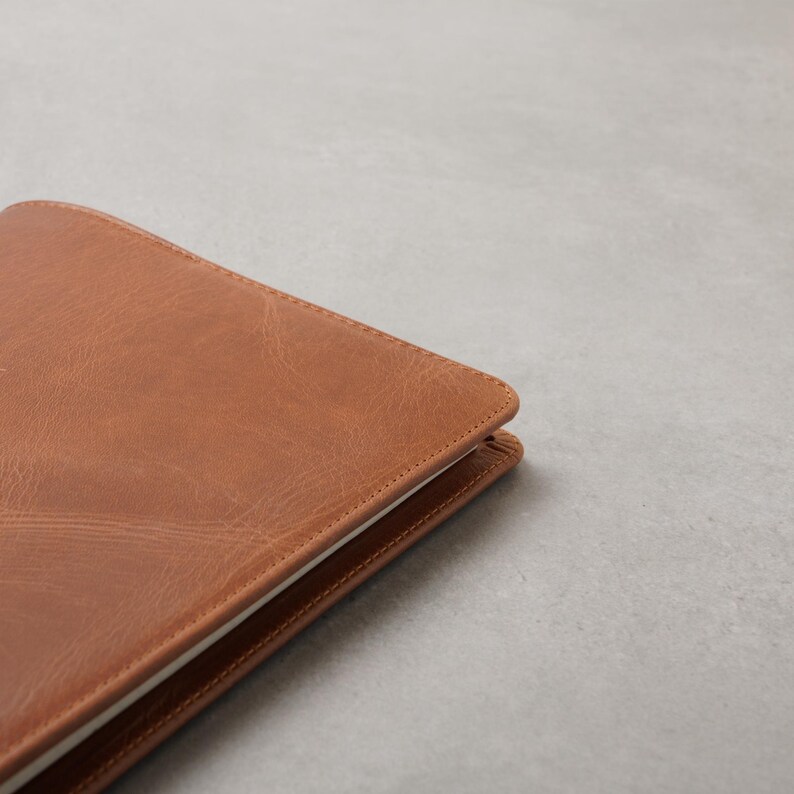 Peut inclure: Gros plan sur un journal en cuir marron avec une bordure cousue. Le journal est ouvert, r&eacute;v&eacute;lant des pages blanches. La couverture a un aspect textur&eacute; et une teinte chaude et terreuse.