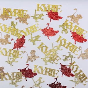May include: Gold and red glitter confetti with the name "Kyrie" repeated on each piece. The confetti is shaped like lions, stars, and other abstract shapes.