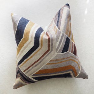 May include: A decorative throw pillow with a geometric pattern in shades of brown, beige, gray, and blue.